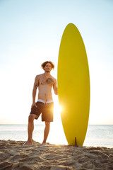 Smiling surfer holding surf board while standing at the beach