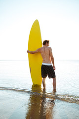 Man with his surfboard standing and looking at the horizon