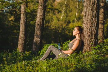 Fitness woman sitting near a tree in the woods resting after a workout. Sport, Fitness, lifestyle concept