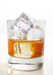 Whiskey with ice cubes in glass on white bg