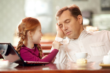 Little daughter bothering her father falling asleep in cafe