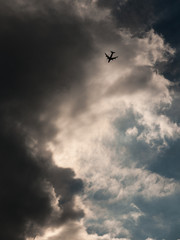 small silhouette airplane in front of towering clouds