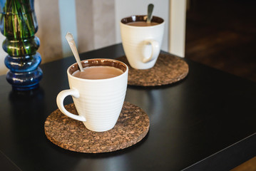 two cups of hot drink near bouquet of flowers in vase on table in apartment