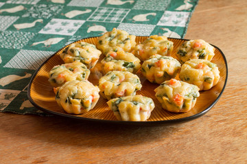 Muffins with salmon, spinach and cheese a big brown plate on green tablecloth with gooses on wood table.