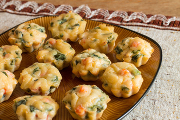 Muffins with salmon, spinach and cheese a big brown plate on tablecloth with pattern on wood table.