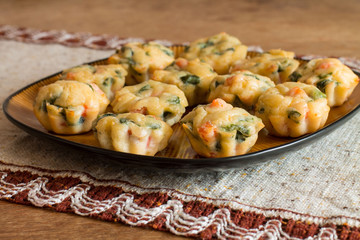 Muffins with salmon, spinach and cheese a big brown plate on tablecloth with pattern on wood table.