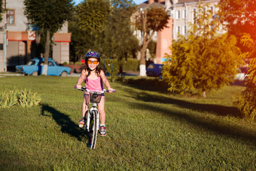 child girl riding bicycle on summer sunset in the park.