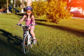child girl riding bicycle on summer sunset in the park.
