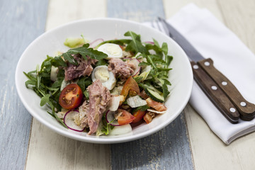 Delicious fresh vegetable salad with tuna on white porcelain plate with fork and knife.