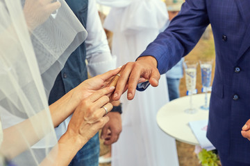 Fototapeta premium Bride putting a wedding ring on grooms finger. Beautiful place for outside wedding ceremony in wood.