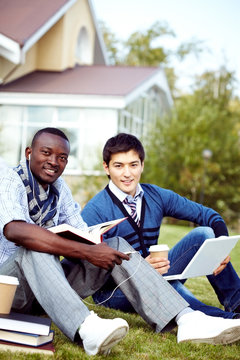 Two young students sitting in campus with textbooks, looking at camera and smiling