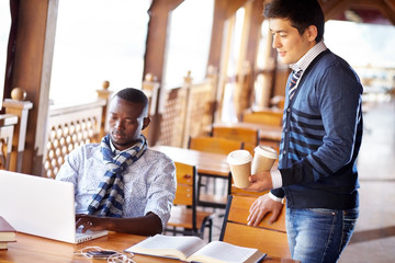 Young man bringing coffee to his friend studying at laptop