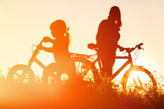 mother and little daughter riding bikes at sunset