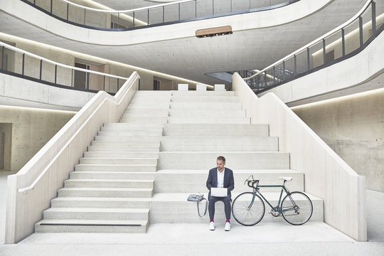 Businessman on stairs using laptop next to bicycle