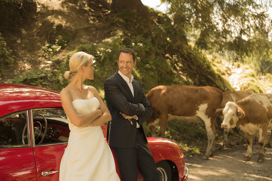 Bridal couple with vintage car waiting on a dirt track