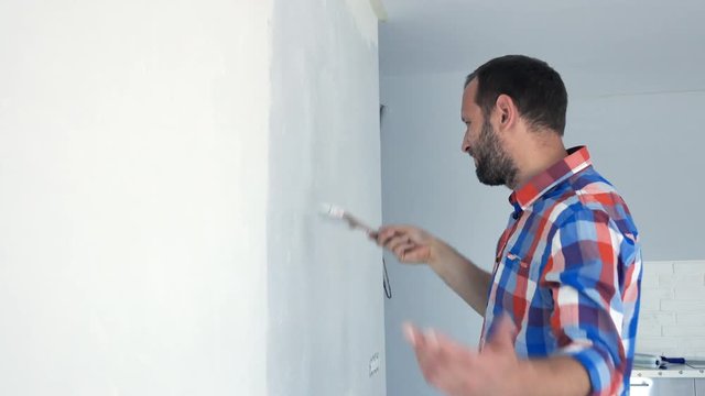 Unhappy, hipster man painting wall at his new home
