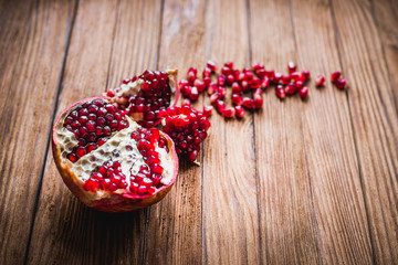 Ripe pomegranate fruit with slices of pomegranate on a wooden table closeup.