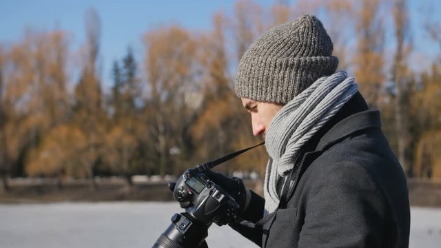 Young man Photographer With professional Camera Equipped in Black Parka Taking Pictures of Beautiful Winter park