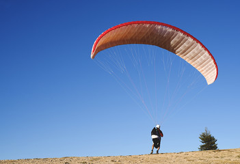 Back view of professional paraglider on ground with flying bright parachute in blue sky