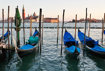 Fototapeta na wymiar The gondolas docked at the pier the Piazza San Marco in Venice, Italy at sunset. In the background is Church of San Giorgio Maggiore. 