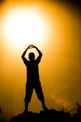 Silhouetted friend forming a heart symbol at golden hour sunset