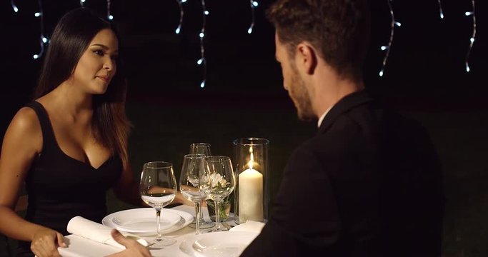 Surprised woman looks questioningly at husband across restaurant dinner table at night