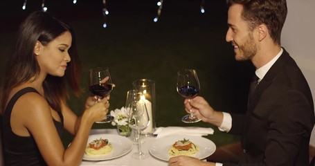 Elegant attractive young couple sipping red wine during a romantic dinner at a nightclub or restaurant - Powered by Adobe
