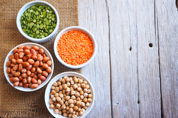Top view of health benefits of dried peanuts, chick peas, red lentils and green peas on a wooden table.