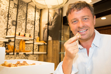 Working place at a bakery. Attractive man with beard tasting bread