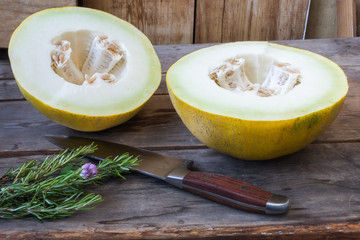 Sliced melon with rosemary and knife on rustic wooden background