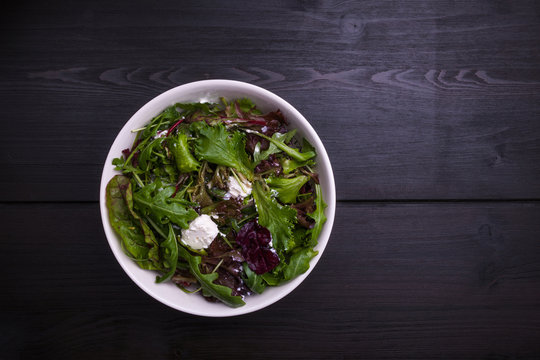 Salad with lettuce and cheese in a white bowl on a black wooden