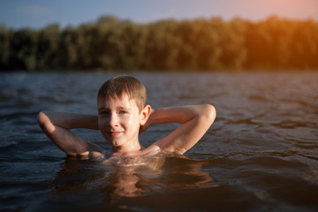little boy swim in blue water at sunset;