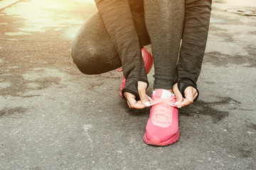 Sporty woman tying the laces on running shoes while taking break between training outside