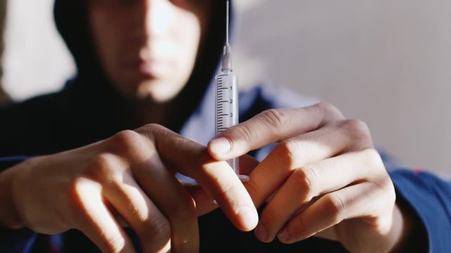 Hands of a man holding a syringe with a drug liuo not in focus. Concept: addiction, willpower to quit addiction