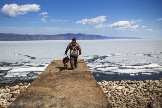 Man walks with his dog near the lake in the spring
