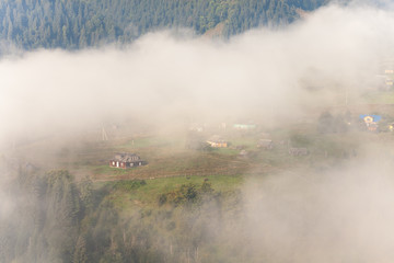 Fototapeta na wymiar Amazing scenery of idyllic countryside with rolling hills veiled in morning fog. Aerial view of a hilltop farmhouse on a foggy spring morning