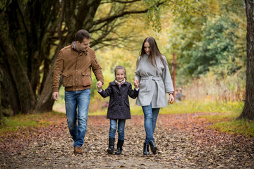 Lovely family walking in the autumn forest. Happy parents enjoying fresh air and beautiful nature, holding hands, talking, smiling and laughing. Healthy lifestyle