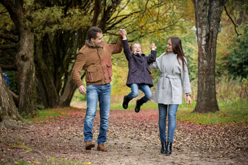 Naklejka na ściany i meble Lovely family walking in the autumn forest. Happy parents enjoying fresh air and beautiful nature, holding hands, jumping and having fun. Talking, smiling and laughing. Healthy lifestyle