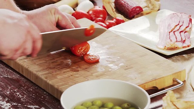 Mens hands cut tomatoes on bamboo cutting board for cooking pizza. Pizza ingredients on wooden background