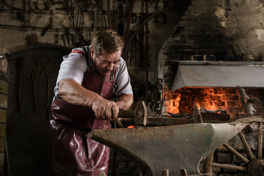 Blacksmith hammering on red hot pick on anvil 