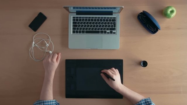 Top view designer man or illustrator uses his graphics tablet and laptop creating digital design and shows thumbs up at the end