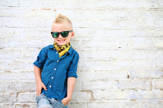стильный мальчик в солнцезащитных очках возле кирпичной белой стены