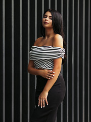 Portrait of young beautiful curvy woman plus size in striped top and black skirt over vertical striped background