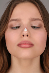 Girl with cream on her nose. Close up. Gray background
