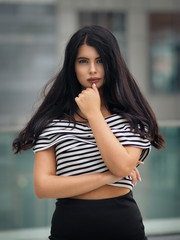 Portrait of young beautiful curvy woman plus size in striped top and black skirt over blurred city background