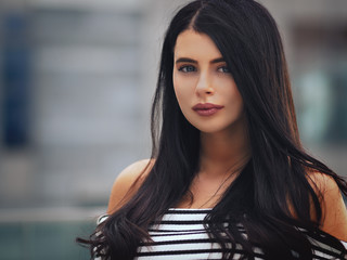 Portrait of young beautiful curvy woman plus size in striped top and black skirt over blurred city background