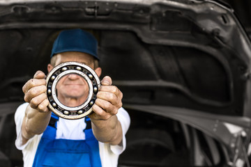 Mechanic holding a bearing. Technician with a blue workwear. Аuto repair garage, auto spare part. Background.
