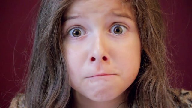 A little girl with an extremely loose tooth plays with it with her tongue and contemplates pulling it with fear in her eyes.