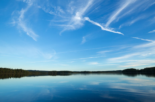 A calm lake in sweden, trails after airplanes in the sky