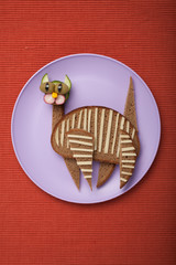 Funny cat made of bread and vegetables on fabric background